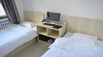 A hotel room with two single beds, a desk with a computer, and a window with curtains.