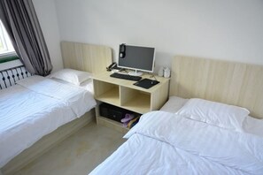 Una habitación de hotel con dos camas individuales, un escritorio con ordenador y una ventana con cortinas.