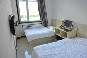Habitación de hotel con dos camas individuales, un escritorio con computadora, un radiador y una ventana con cortinas.