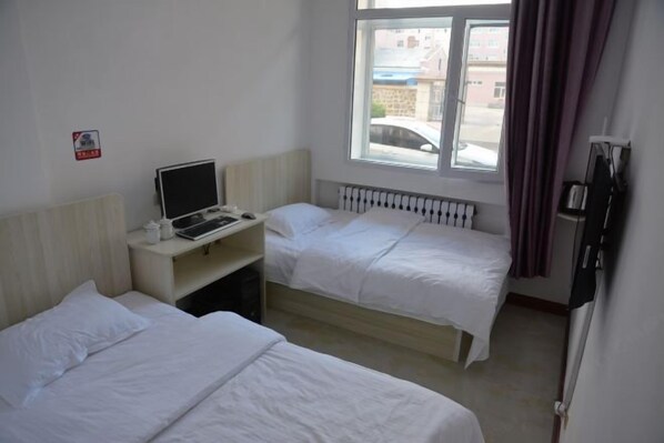 Une chambre d’hôtel avec deux lits, un bureau avec un ordinateur, une fenêtre donnant sur la rue et un radiateur.