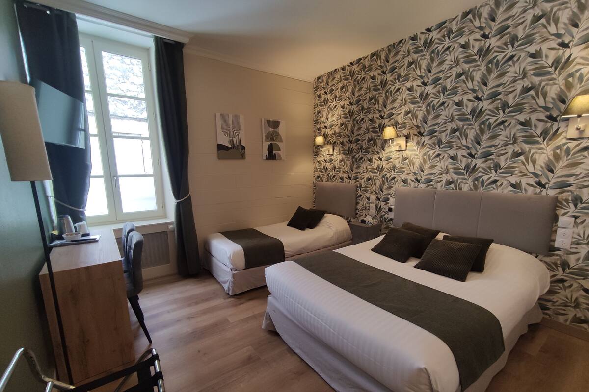 A hotel room with two beds, a desk, a chair, a window with curtains, and a wall with a leaf pattern.