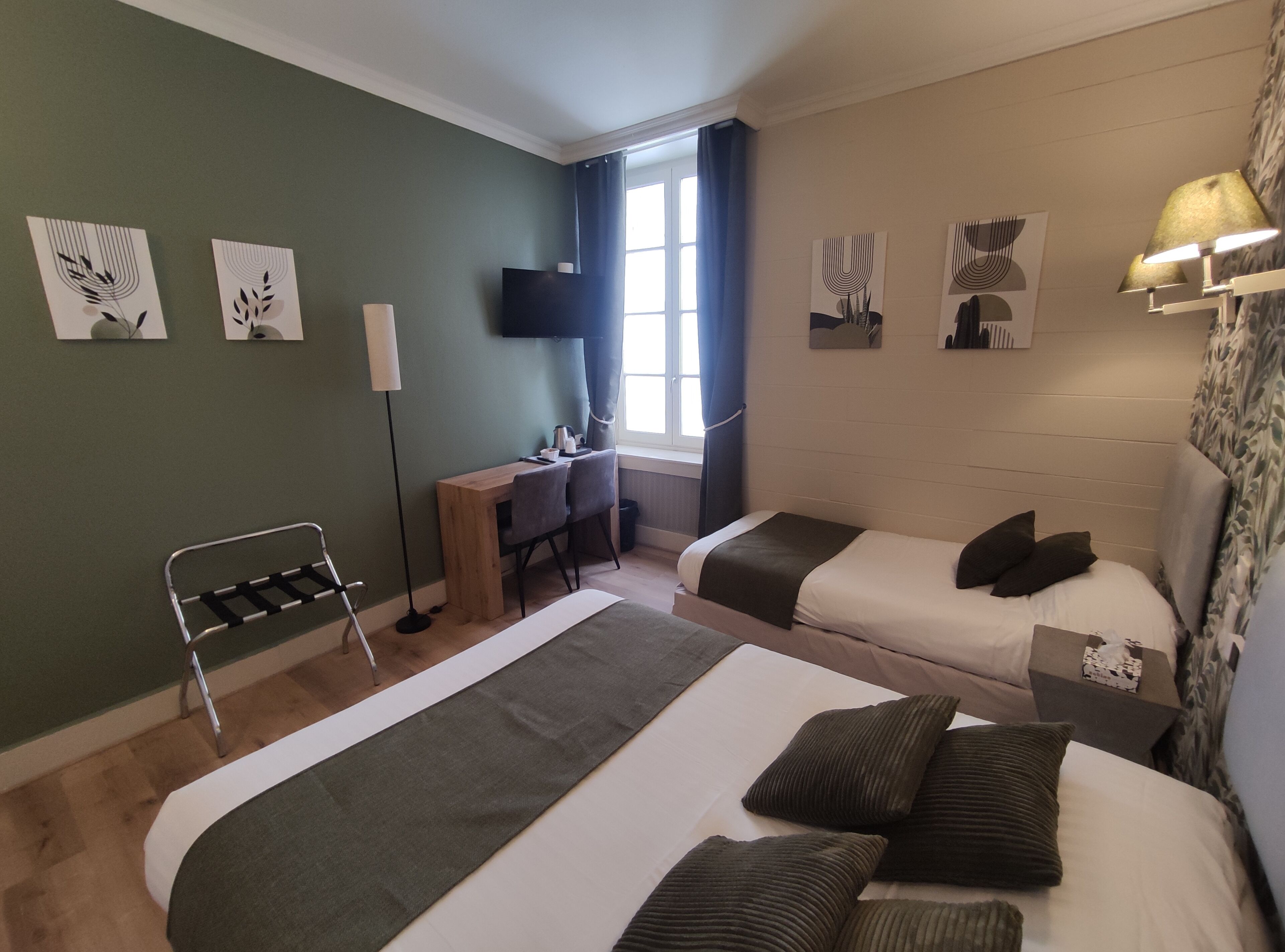 A hotel room with two beds, a desk, a chair, a TV, and artwork on the walls.