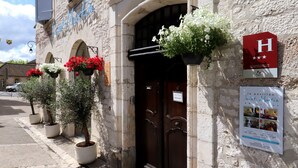 Um edifício histórico com fachada de pedra, porta de madeira e caixas de flores com flores vermelhas e brancas.