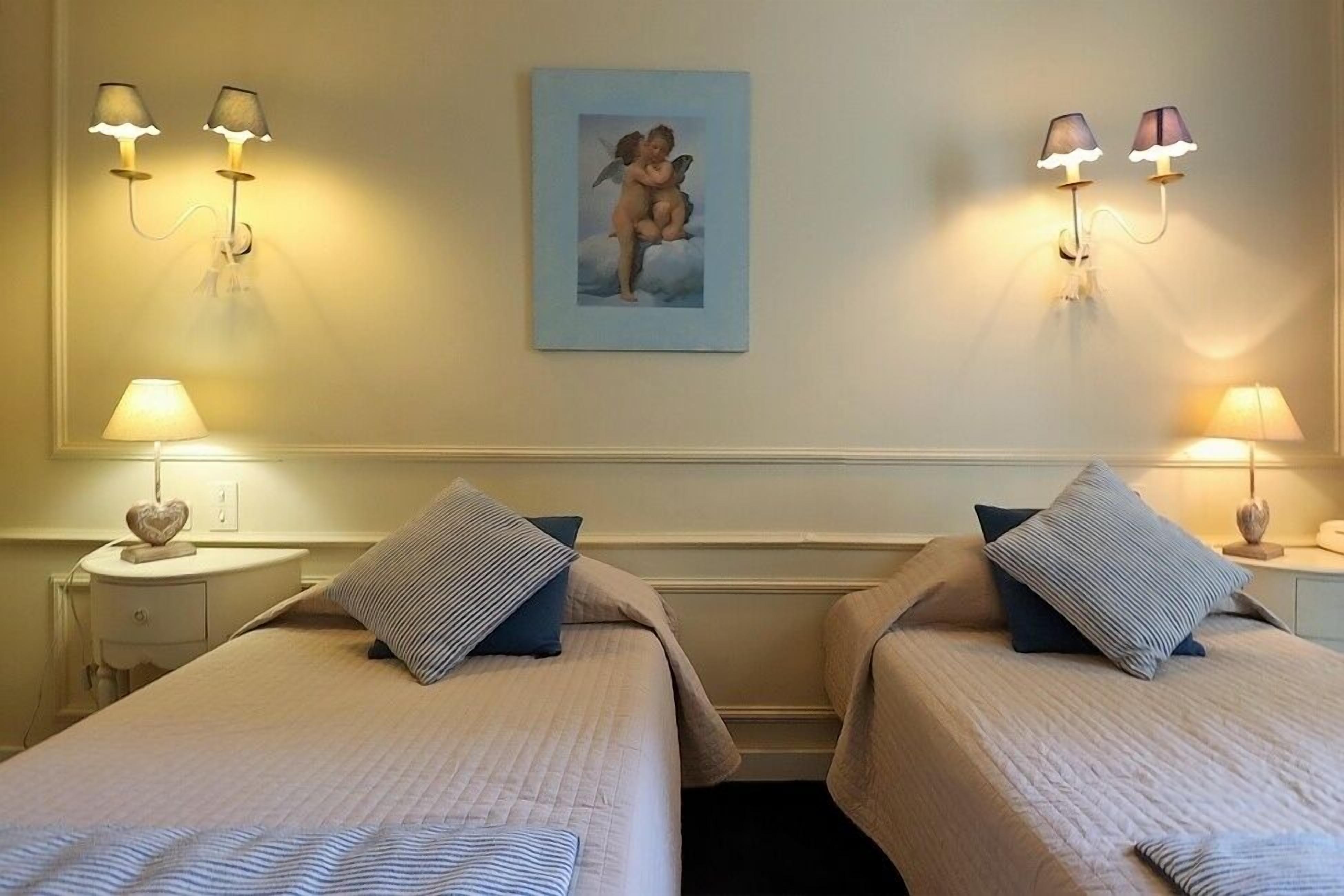 Habitación de hotel con dos camas, cada una con un cojín y un objeto con forma de corazón en la mesita de noche.