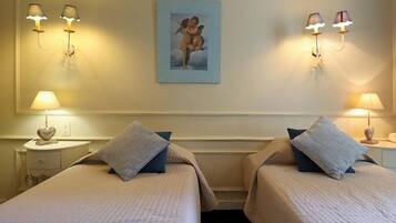 Habitación de hotel con dos camas, cada una con un cojín y un objeto con forma de corazón en la mesita de noche.