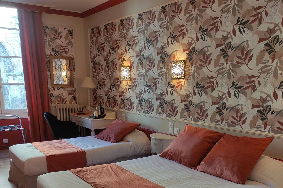 A hotel room with two beds, a desk, a chair, and a radiator.