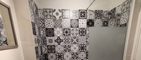 Un baño con lavamanos blanco, cabina de ducha con mampara de vidrio y azulejos decorativos en las paredes.