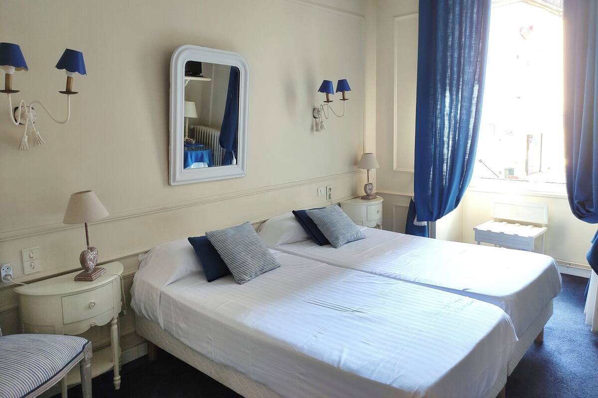 A hotel room with two beds, a large mirror, bedside lamps, and a view of the outside.