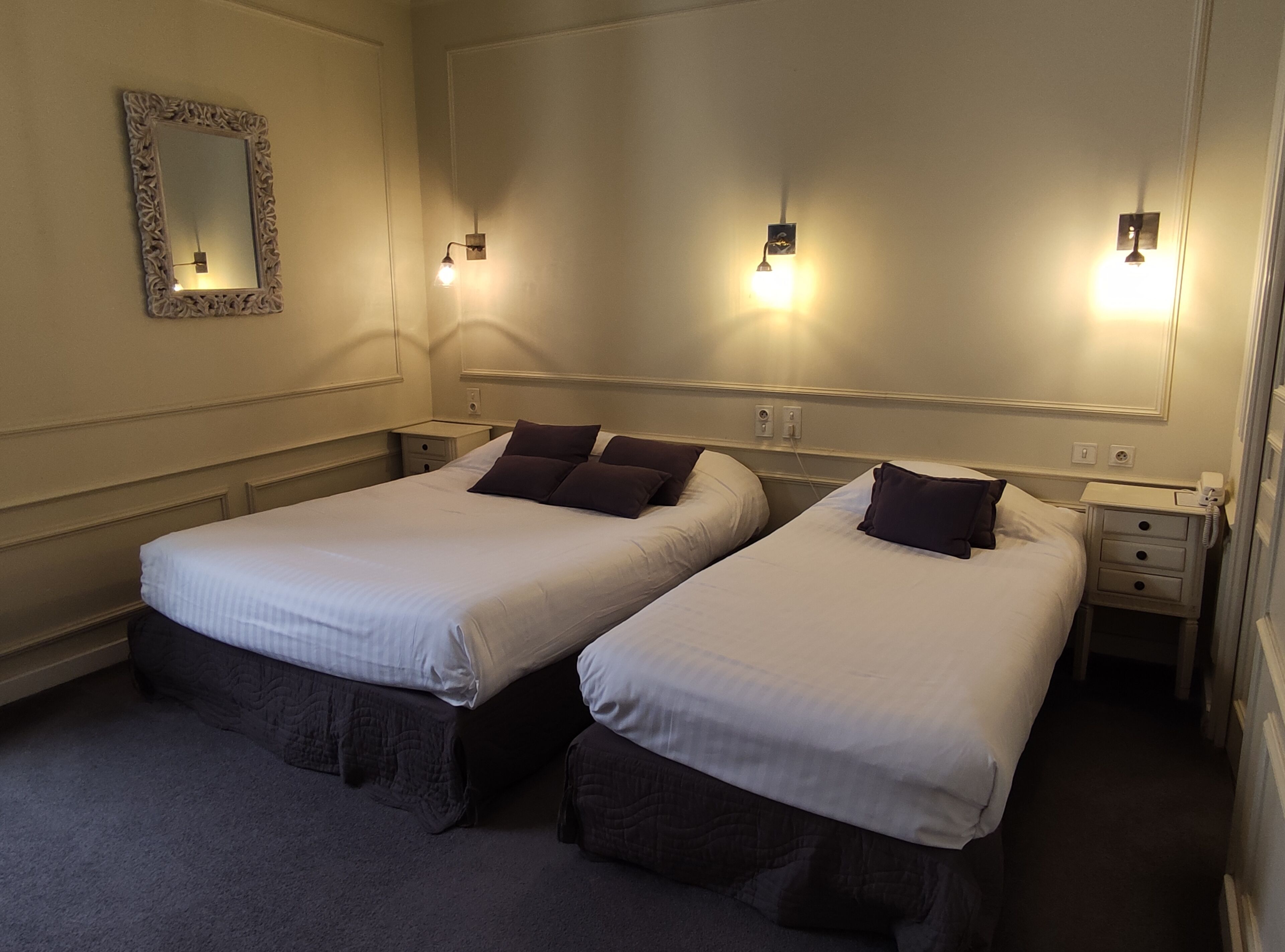 A hotel room with two single beds, a large mirror, and wall-mounted reading lights.
