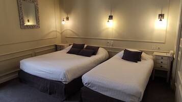 A hotel room with two single beds, a large mirror, and wall-mounted reading lights.