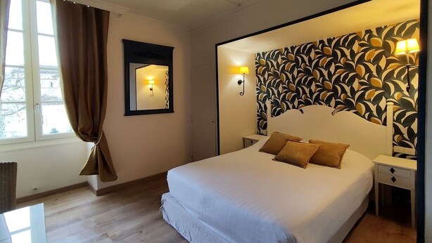 A bedroom with a large bed, a mirror, a patterned wall, and a window with curtains. - Le Pavillon Saint Martin (Souillac)
