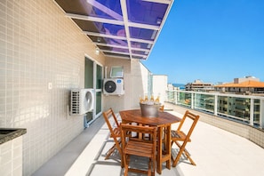 Terraza en la azotea con mesa y sillas de madera, unidades de aire acondicionado y una barandilla de cristal con vistas a la ciudad.