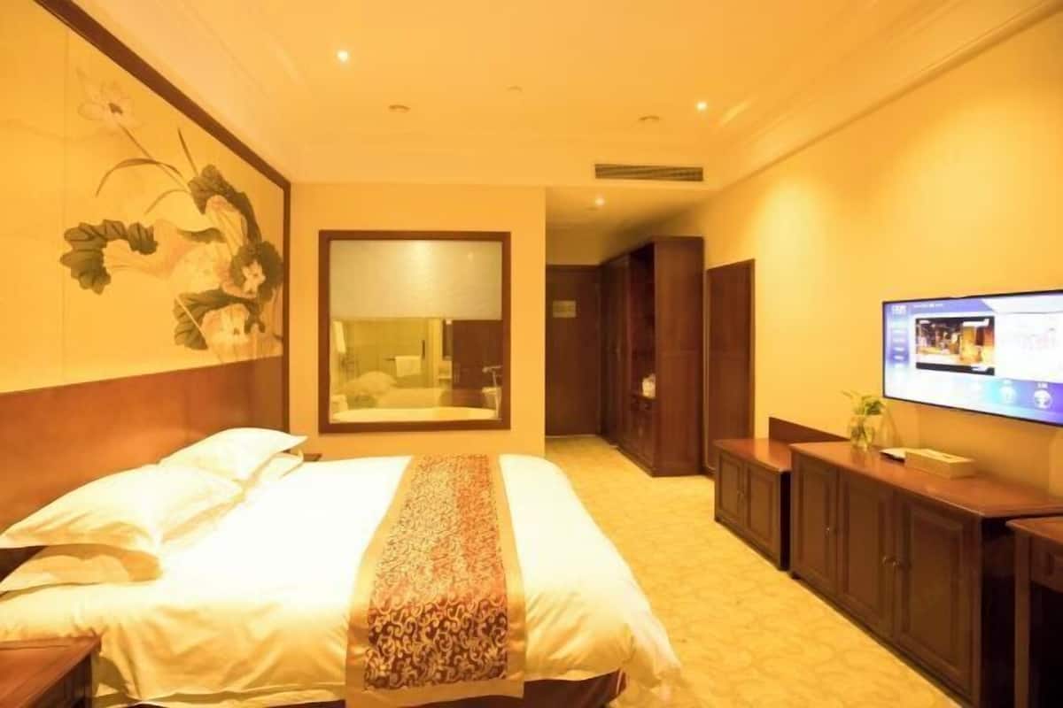 Une chambre d’hôtel avec un grand lit, une télévision, un miroir et une armoire en bois.