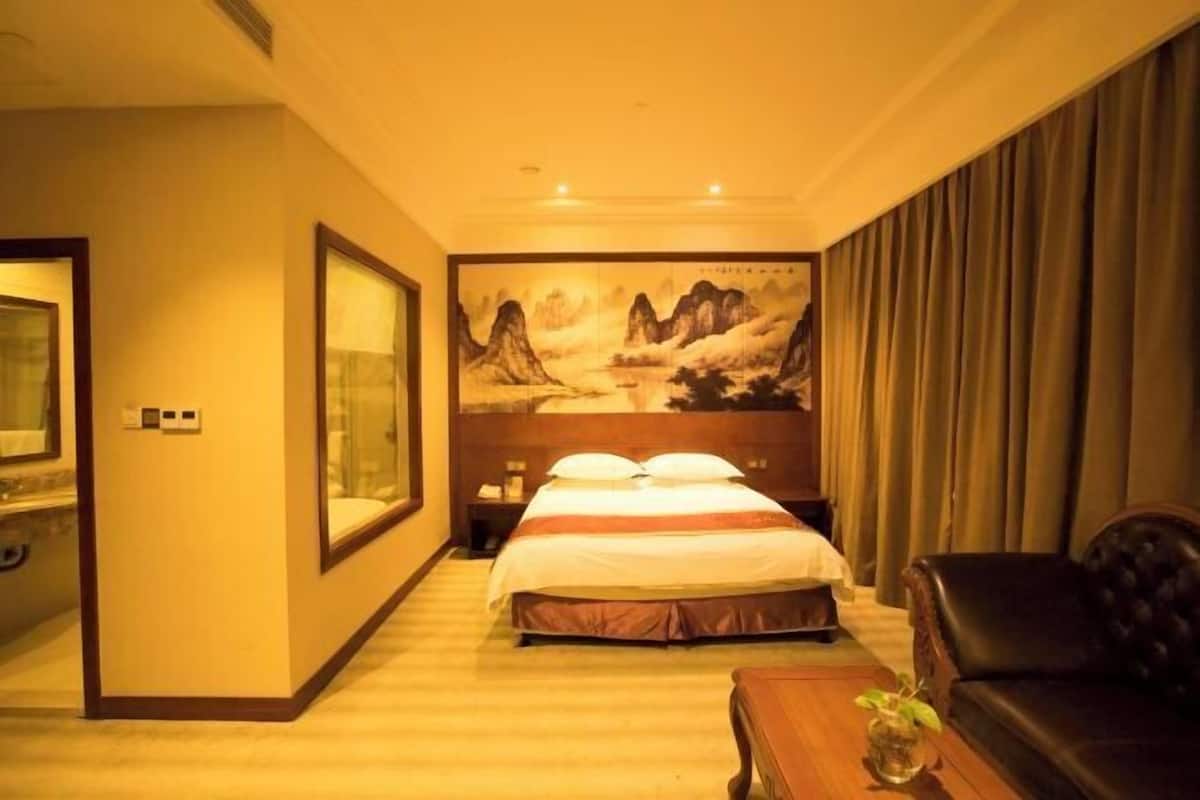 Une chambre d’hôtel avec un lit, une télévision, un grand tableau et un canapé en cuir.
