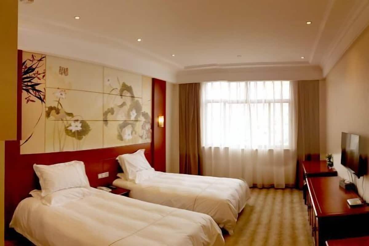 Une chambre d’hôtel avec deux lits, une télévision, un bureau et une grande fenêtre avec des rideaux.
