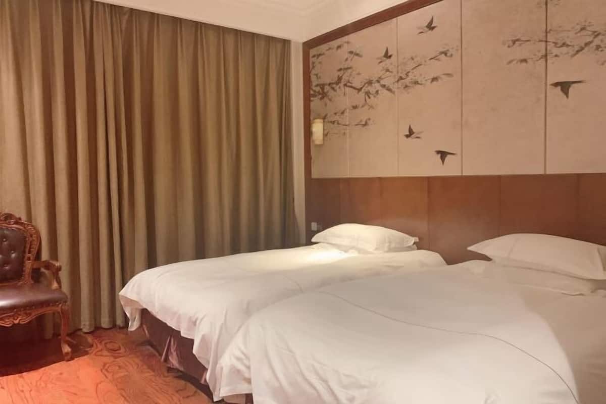 Une chambre d’hôtel avec deux lits, une tête de lit en bois, une grande fenêtre avec des rideaux et un mur orné d’une fresque représentant des oiseaux.