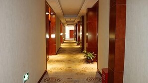 En hotellkorridor med ett mönstrat golv, trädörrar och krukväxter.