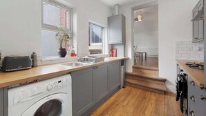 A modern kitchen with grey cabinets, a built-in washing machine, a toaster, and a window with a plant. - Central Newcastle 2BR with Free Parking and Wifi (Tyne and Wear)