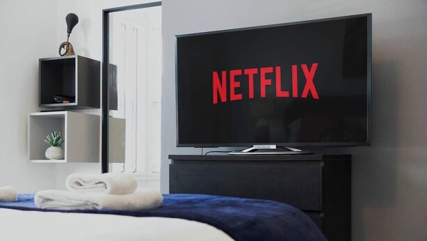 A modern hotel room with a bed, a TV displaying 'NETFLIX,' and a small shelf with a plant. - Central Newcastle 2BR with Free Parking and Wifi (Tyne and Wear)
