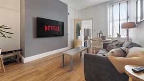 A modern living room with a flat-screen TV mounted on the wall, a bench, a sofa, and a lamp. - Central Newcastle 2BR with Free Parking and Wifi (Tyne and Wear)