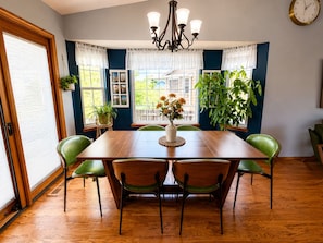 A dining room with a wooden table, four chairs, a chandelier, and large windows with curtains.