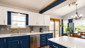 A modern kitchen with white and blue cabinets, a stainless steel dishwasher, and a large island with a white countertop. - Prairie Peace - Family & Pet-Friendly Home on Quiet Cul-De-Sac w/ Games & Toys (Wichita)