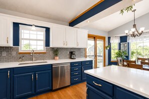 A modern kitchen with white and blue cabinets, a stainless steel dishwasher, and a large island with a white countertop.