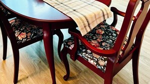 Un comedor con una mesa de madera, sillas con estampado floral, una servilleta de mesa a cuadros y una escalera con barandillas de madera.