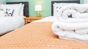 A hotel room with two beds, a nightstand with a lamp, and a folded towel on the bed.