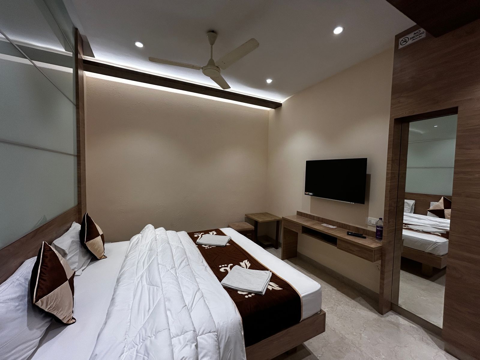 Una habitación de hotel moderna con cama, televisión, mesita de noche y espejo.