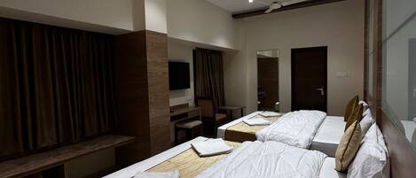 A hotel room with three beds, a ceiling fan, recessed lighting, a TV, and a large mirror.