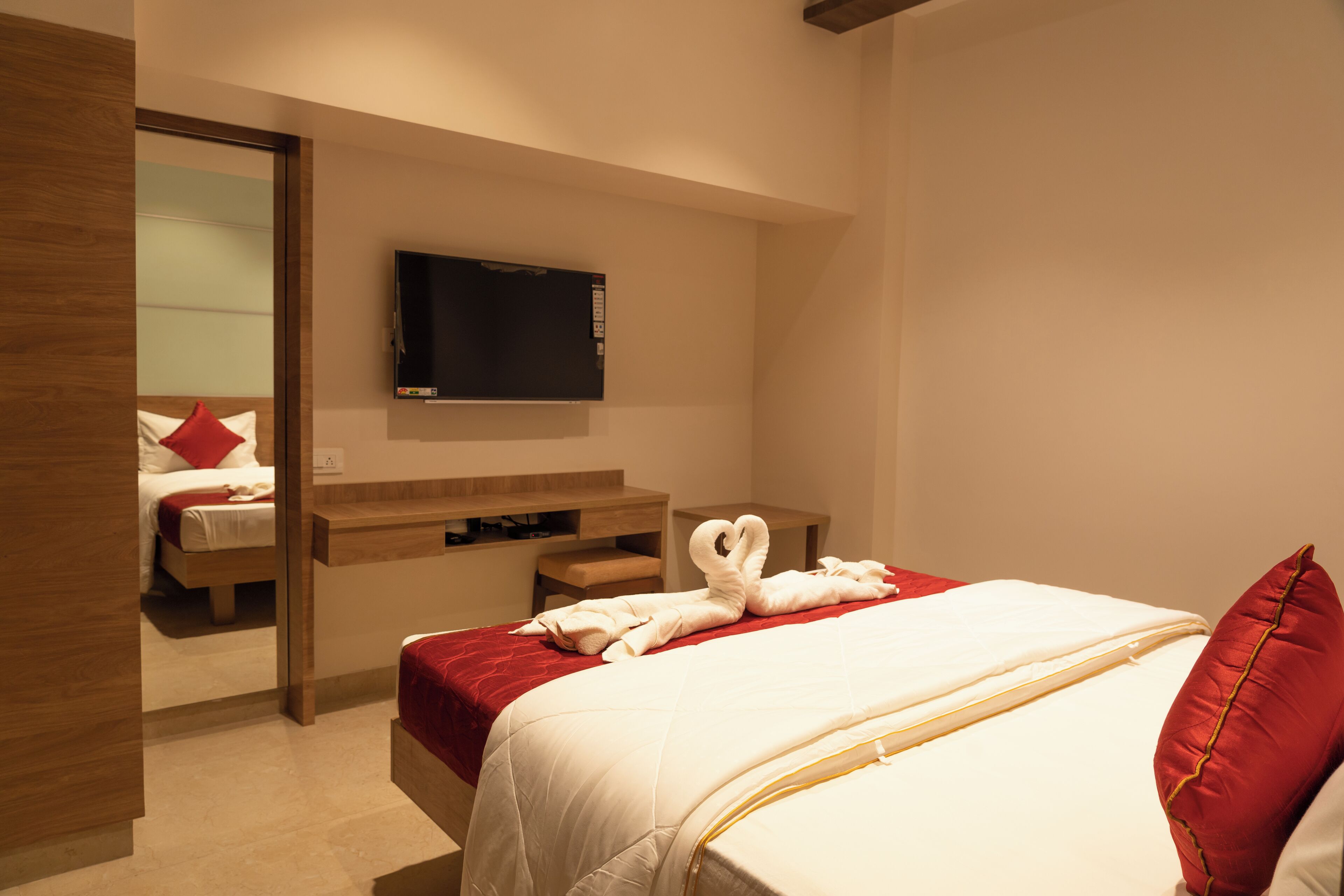 A hotel room with a bed, a TV mounted on the wall, and a wooden bench.