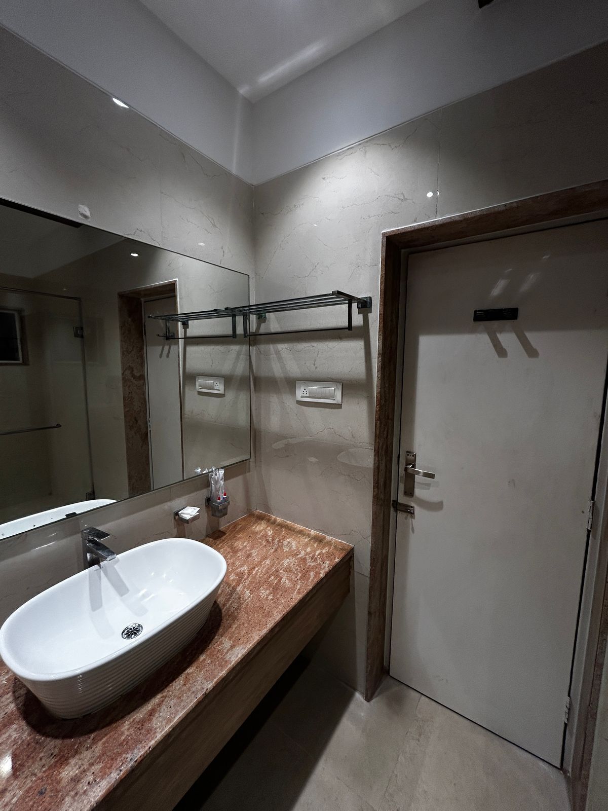 Un baño moderno con un espejo grande, un lavamanos blanco y una puerta.