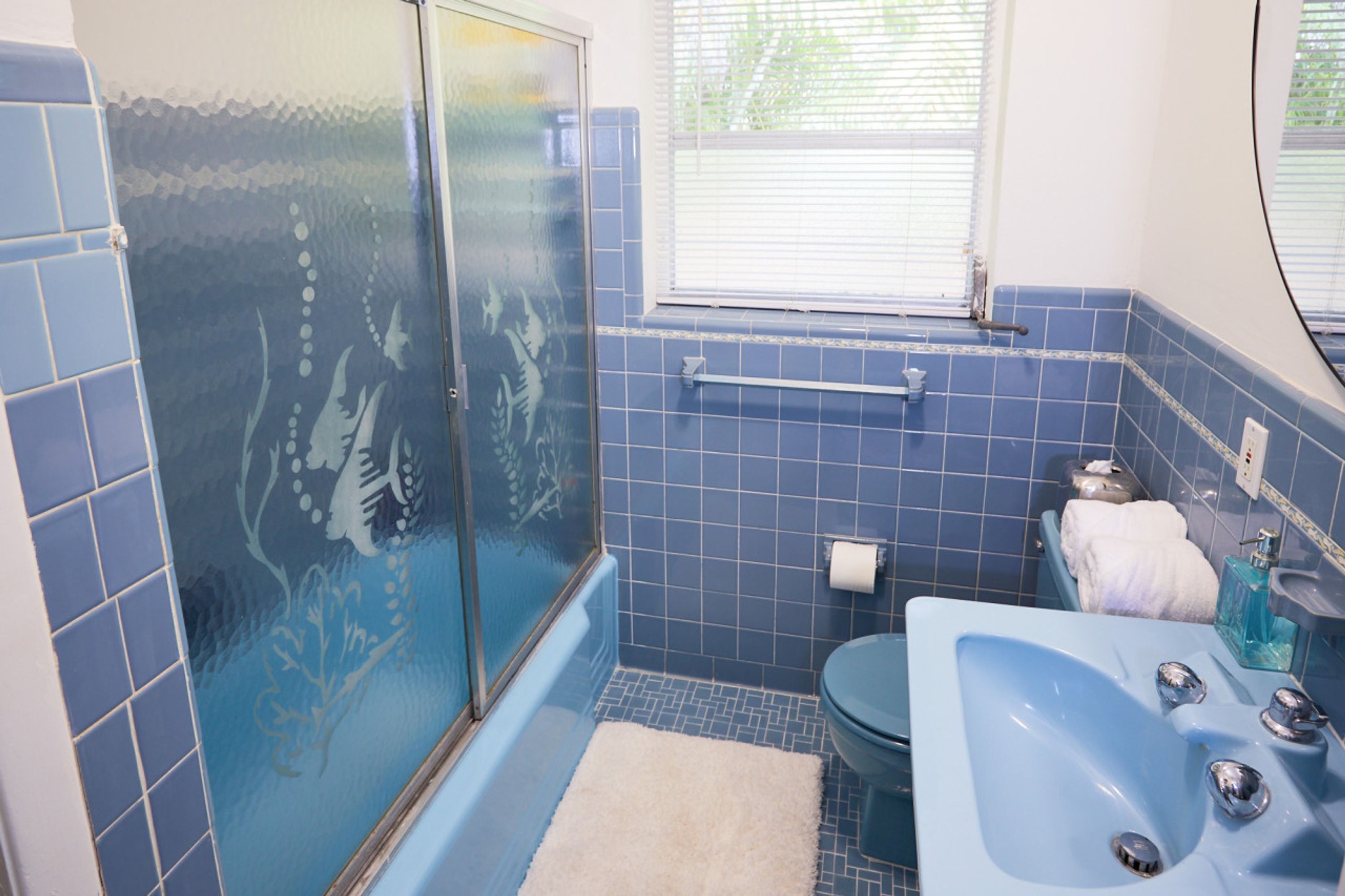A bathroom with a blue tiled wall, a glass shower enclosure, a white sink, and a toilet.