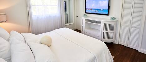 A bedroom with a bed, a TV on a stand, a mirror, and a closet.