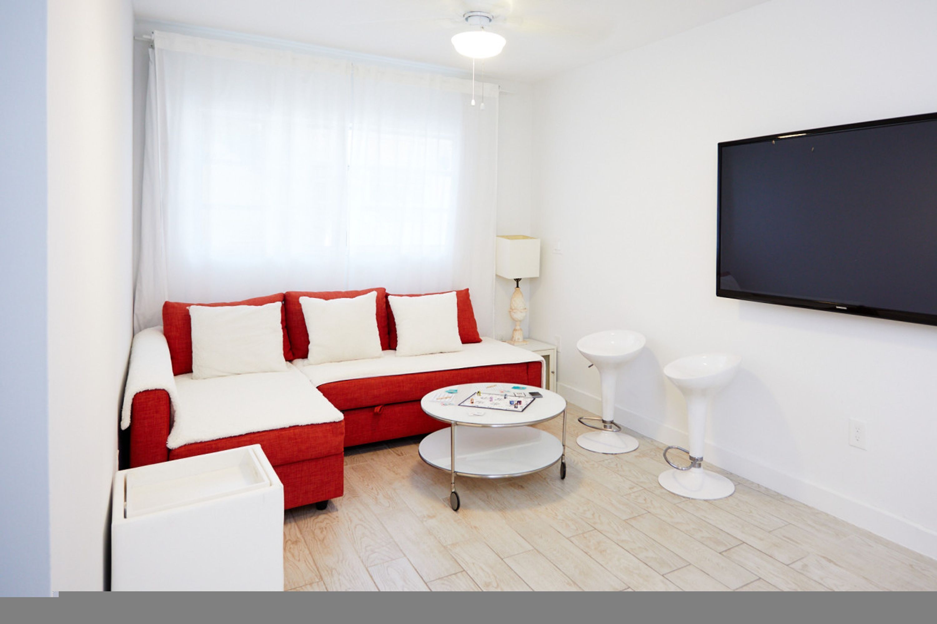 Egy modern szállodai szoba, melyben piros kanapé, egy kis, kerek asztal, televízió és fehér lámpa található.