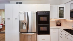 Eine moderne Küche mit einem Edelstahl-Kühlschrank, einem Backofen mit Platz für zwei Auflaufformen und weißen Schränken.