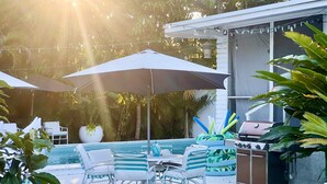 A poolside area with a barbecue grill, outdoor seating, and umbrellas. - Miami Pool Cottage in El Portal (Miami)