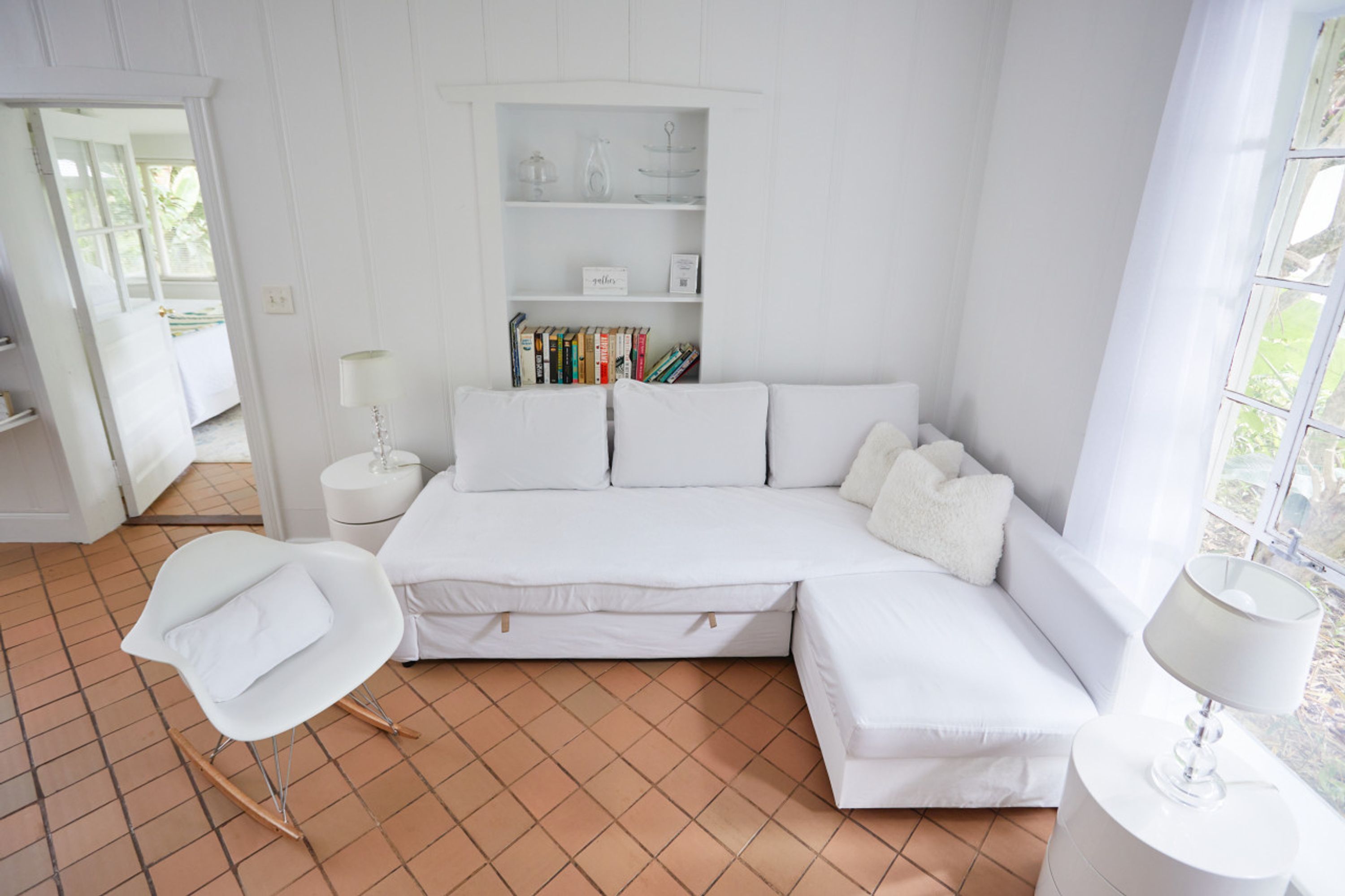 A white room with a sofa, a chair, a bookshelf, and a window.