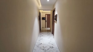 A hallway with marble flooring, beige walls, and a wooden door at the end. - Hotel Prime Suites Airoli (Navi Mumbai)