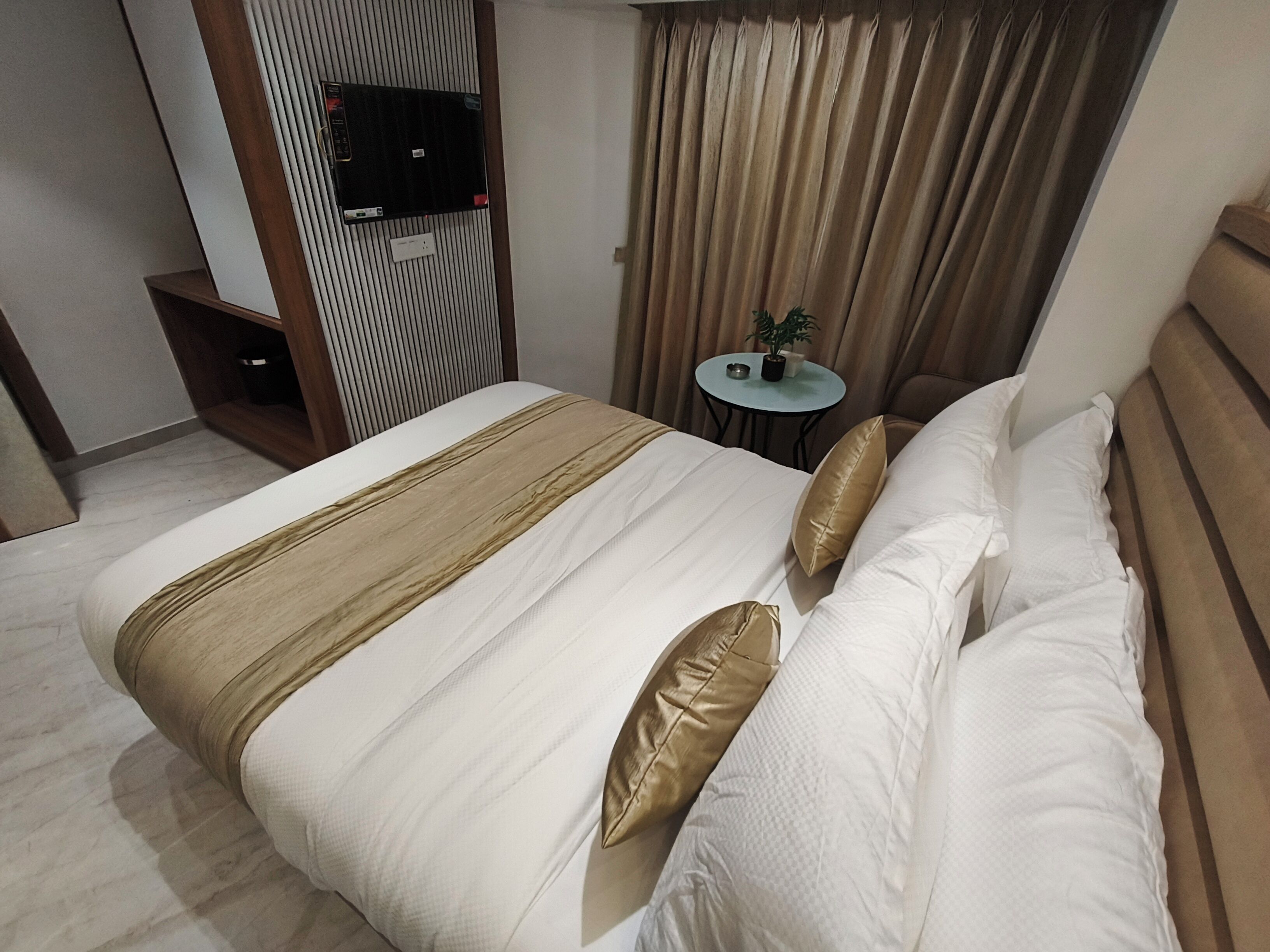 Una cama bien hecha con una colcha a rayas, dos almohadas y una pequeña mesa redonda con una planta a su lado.