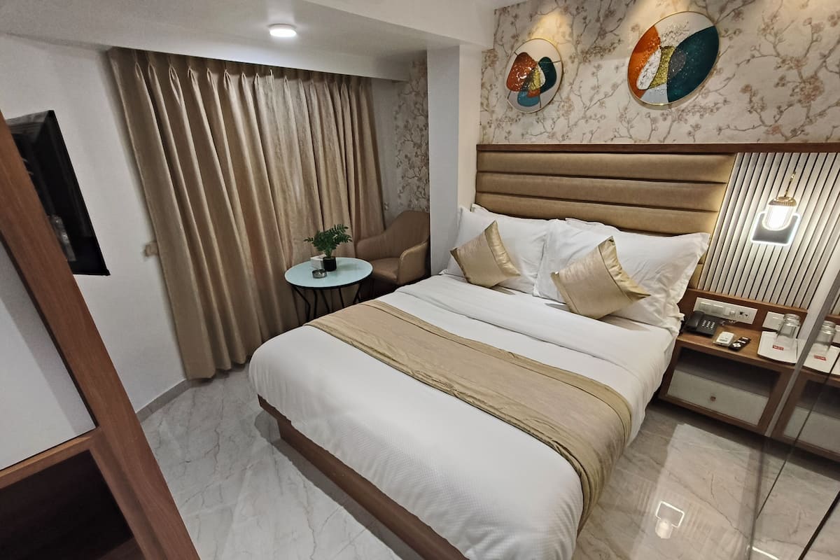 A hotel room with a large bed, a bedside table with a lamp, a small round table with a plant, and a sofa.