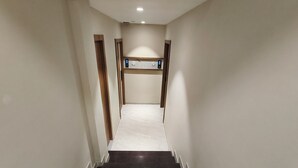 A narrow, well-lit hallway with dark marble steps leading to a landing with a wooden railing and a white floor. - Hotel Prime Suites Airoli (Navi Mumbai)