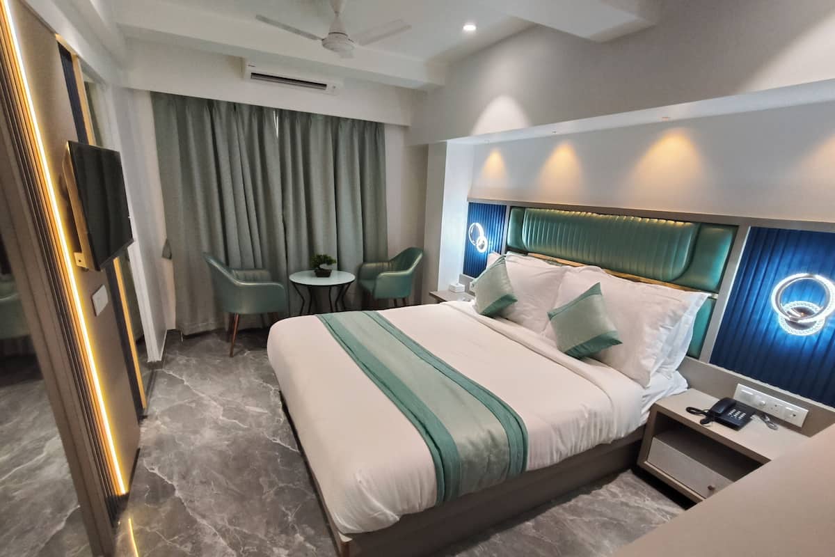 A modern hotel room with a large bed, a desk with a phone, a chair, a small table with a plant, and a ceiling fan.