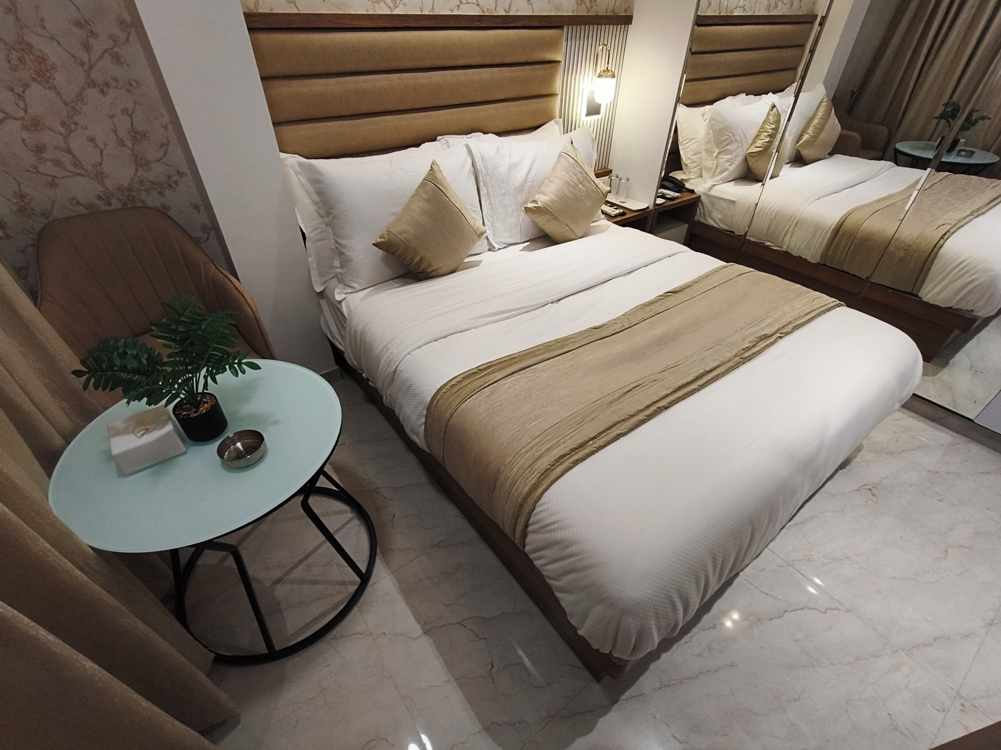 A hotel room with two beds, a small round table with a plant, and a chair.