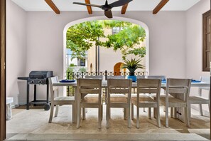 A dining area with a table and chairs, a ceiling fan, and a view of greenery through an arched window. - Beach Villa las Catalina’s (Las Catalinas)