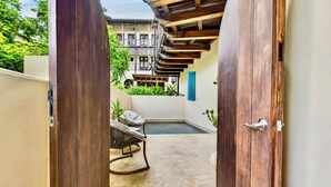 Un patio estrecho con una puerta de madera, una silla metálica y una pequeña piscina.