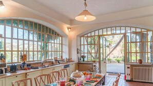 A spacious kitchen with large windows, a dining table set for six, and a view of the garden. - Villa la Cicaliera 10, Emma Villas (Sanremo)