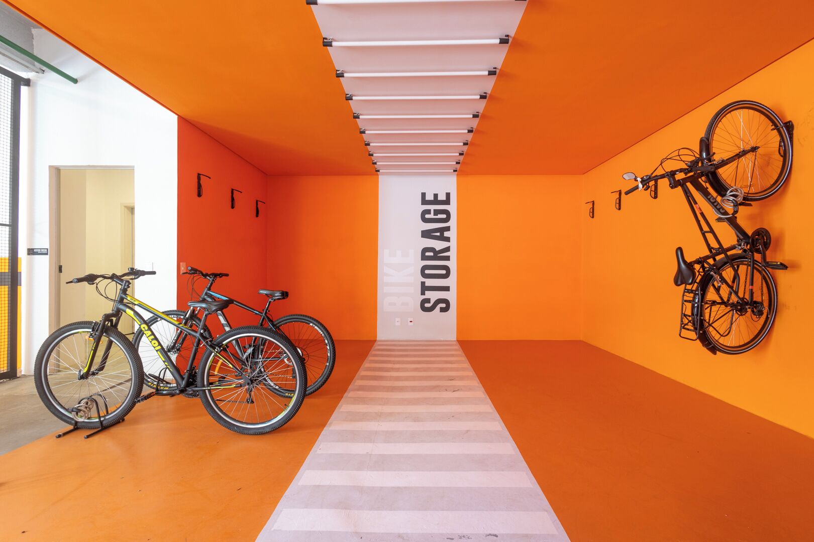 Un almacén bien iluminado con paredes anaranjadas y suelo blanco, que muestra bicicletas y un gran letrero que dice 'STORAGE'.