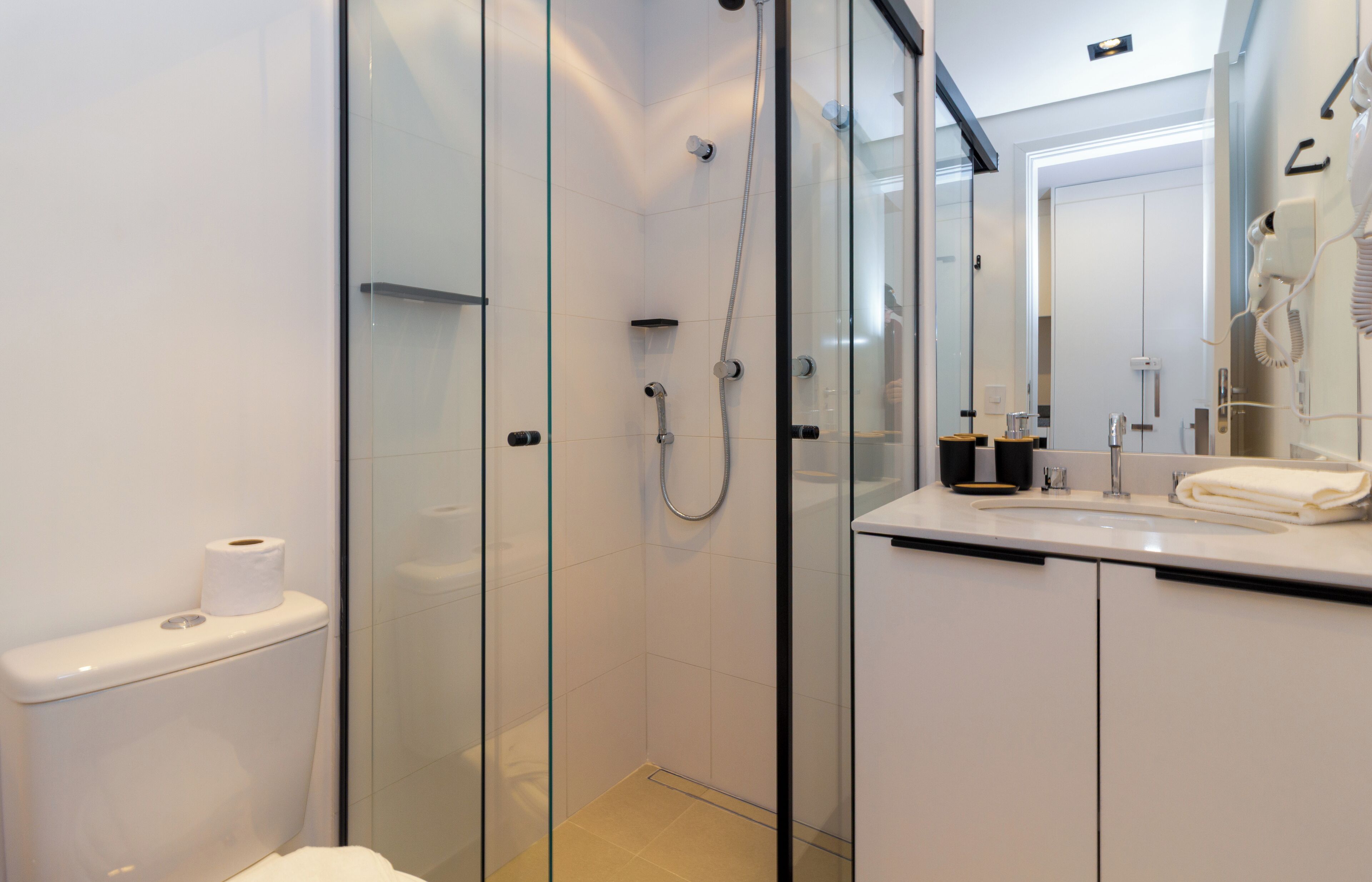 Une salle de bain moderne dotée d’une douche à parois de verre, de toilettes, d’un lavabo avec une serviette et d’un sèche-cheveux fixé au mur.